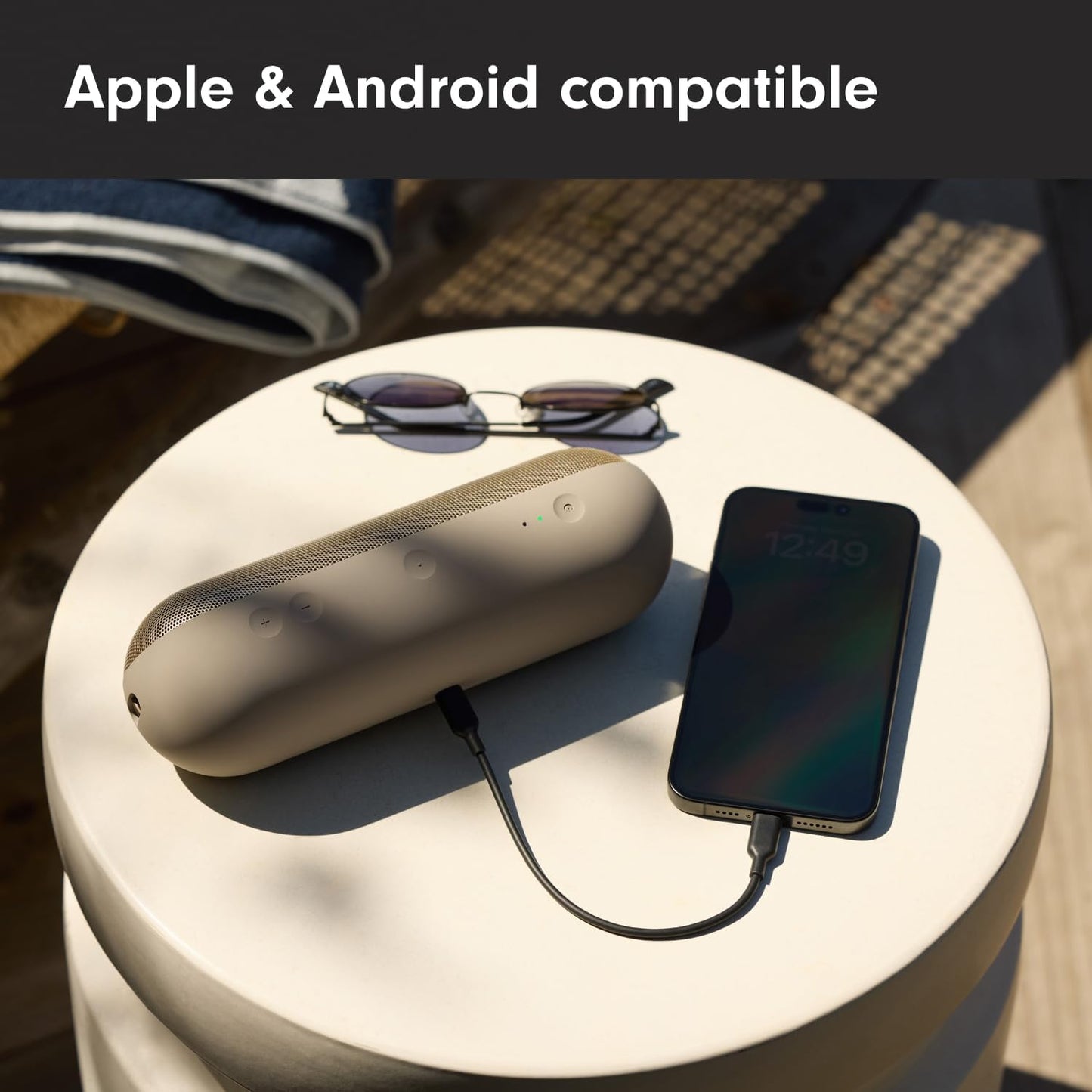 Beats Pill Bluetooth Speaker in beige on a table with sunglasses and a phone connected